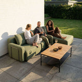 Grøn modulopbygget loungesofa fra sackit på terrasse med tre personer og sofabord i træ i en solrig have