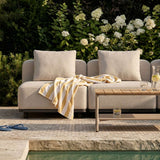 Beige udendørs hjørnesofa fra sackit på terrasse ved pool med bløde puder et stribet tæppe og lavt træbord omgivet af grønne planter
