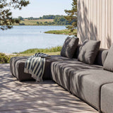 Grå modulopbygget loungesofa med chaiselong på træterrasse ved søen med bløde puder og stribet tæppe fra sackit