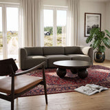 Fjord sofa til tre personer i mørkegråt stof i en lys skandinavisk stue med rundt sofabord mønstret tæppe grøn plante og lænestol