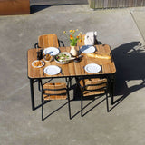 Udendørs spisebord i teak med fire matchende stole fra sackit dækket op med tallerkener brød salat og blomster på en solrig terrasse