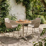 Udendørs cafésæt fra sackit med rundt træbord og to taupefarvede stole på en solrig terrasse omgivet af grønne planter