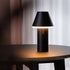 Sort trådløs bordlampe fra sackit med konisk skærm og blødt varmt lys på et mørkt træbord i elegant nordisk interiør