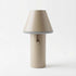 Beige trådløs bordlampe med konisk skærm og cylindrisk fod på lys baggrund. Enkelt nordisk design til indendørs og udendørs brug