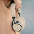 Beige over ear høretelefoner fra sackit holdes i hånden med polstrede ørepuder og blødt hovedbånd i et minimalistisk design