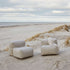 To lyse Soft Sofa Outdoor moduler fra sackit på en sandstrand med klitter og havudsigt den ene med et tæppe over sig