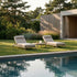 To justerbare Kirra solsenge fra sackit med lyse hynder ved en pool i en grøn have omgivet af træer og moderne arkitektur