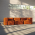 Blød orange indendørs sofa uden stel med fleksible puder i et lyst rum med varme solstriber fra vinduet. Designet af sackit til afslappet komfort