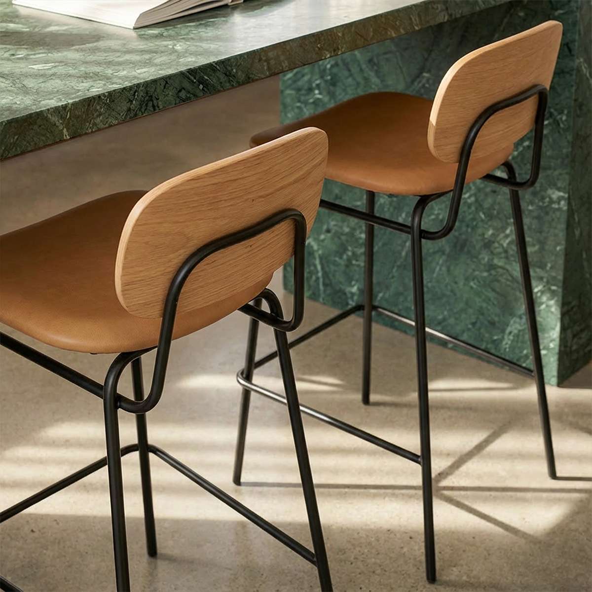 Frame Bar Stool barstol med ryglæn i sort læder og sort pulverlakeret stålstel indendørs.