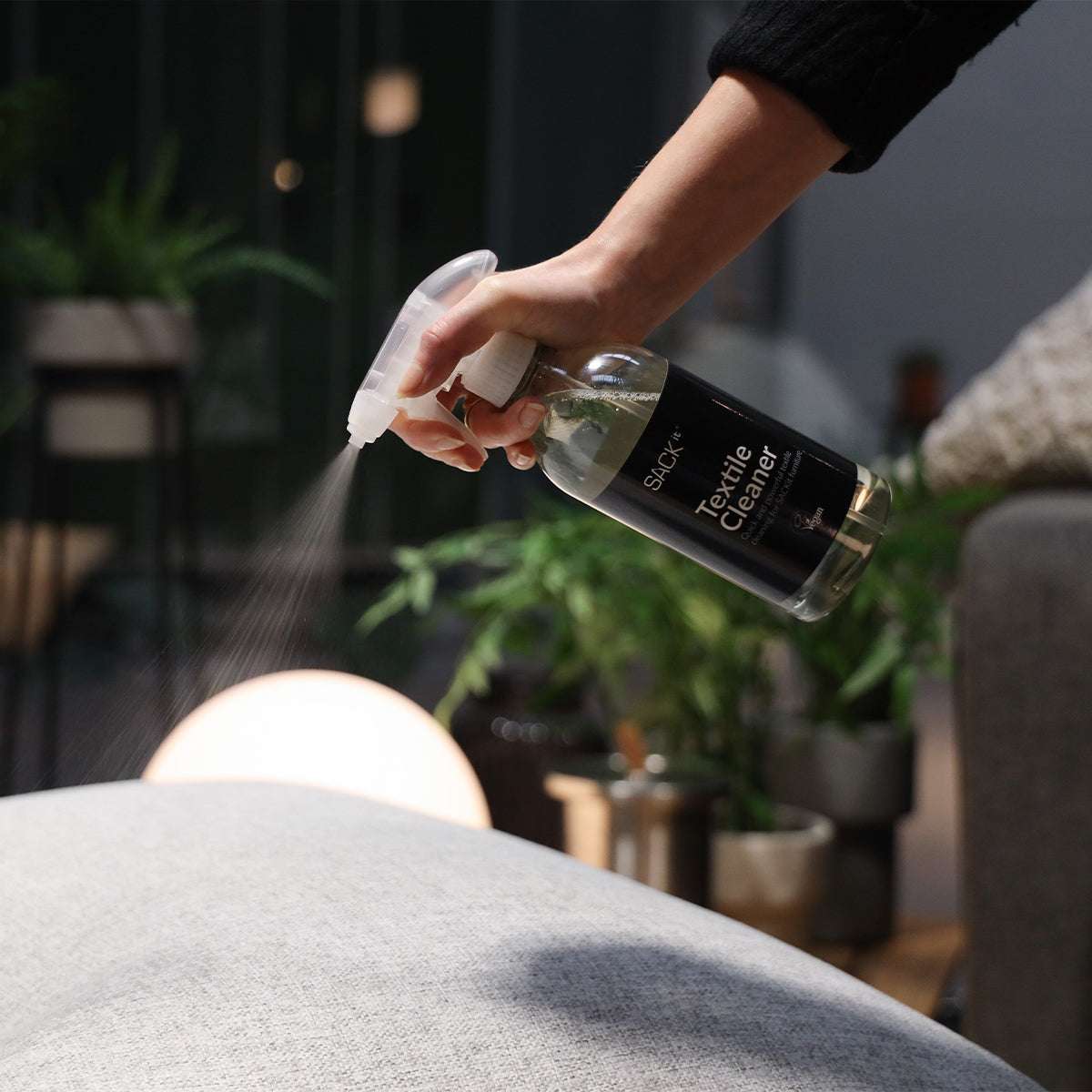 sackit Textile Cleaner sprayes på en lys tekstiloverflade for nem pletfjerning og enkel vedligeholdelse af møbler
