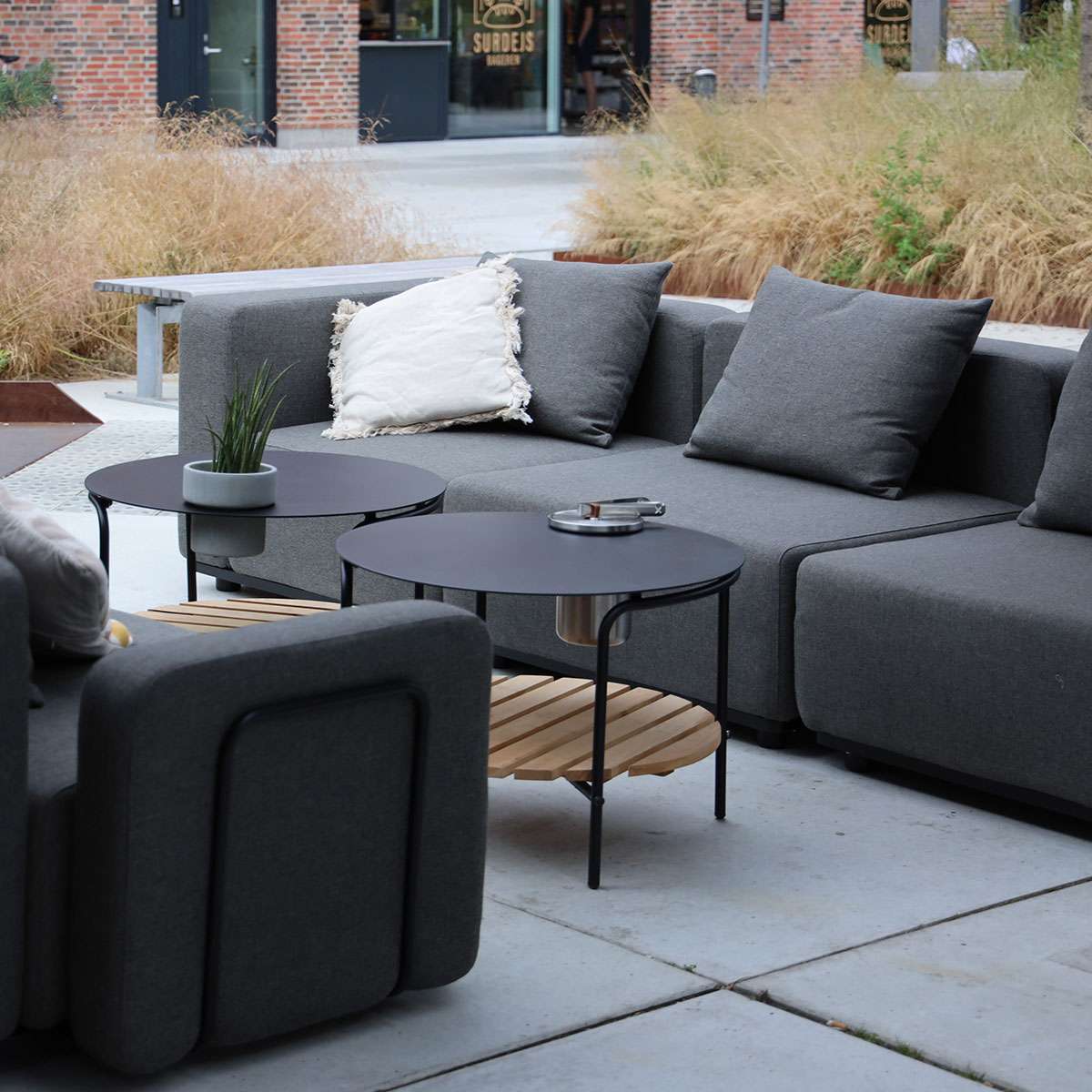Mørkegrå modulopbygget udendørs sofa fra sackit med bløde puder og runde sofaborde på en stilfuld terrasse i nordisk design