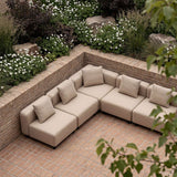 Sandfarvet modulopbygget udendørs loungesofa i et hyggeligt gårdmiljø med murstensbelægning og frodige blomsterbede afspejler sackit designet i Danmark.