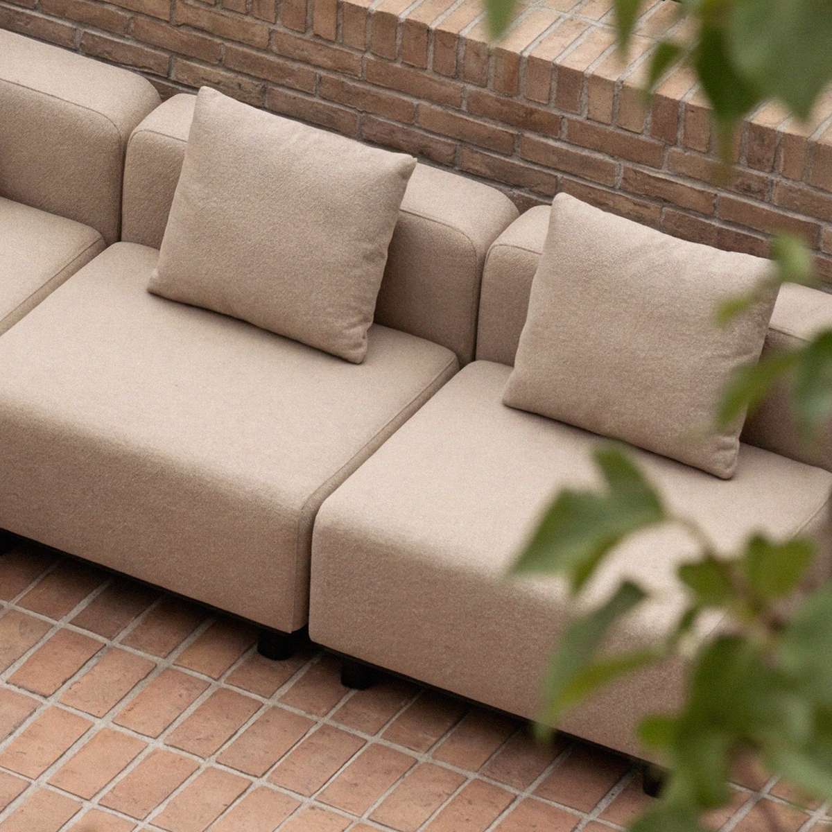 Beige modulopbygget udendørs loungesofa fra sackit med bløde hynder på en terrasse med murstensbelægning og grønne planter