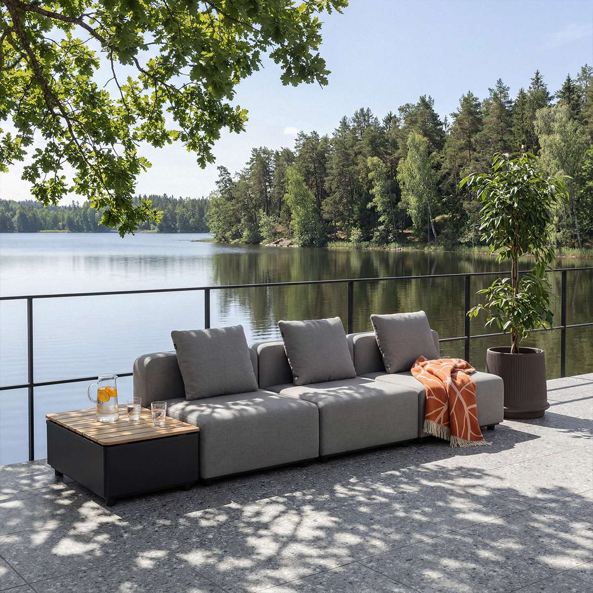 Grå modulopbygget udendørs sofa med bløde puder og orange plaid på terrasse ved søen omgivet af træer dnaisk design fra sackit
