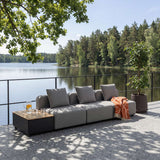 Grå modulopbygget udendørs sofa med bløde puder og orange plaid på terrasse ved søen omgivet af træer dnaisk design fra sackit