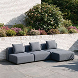 Mørkegrå modulopbygget udendørs loungesofa med puf og puder på en solrig terrasse ved en hvid mur designet i Danmark af sackit