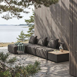 sackit modulopbygget udendørs loungesofa med puf i mørkt tekstil på træterrasse ved vandet med puder og sidebord