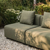 Grøn modulopbygget hjørnesofa fra sackit på en grusbelagt terrasse omgivet af frodige planter og bløde puder i nordisk design