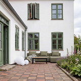 Olivegrøn Cobana loungesofa med tre siddepladser og sofabord på en hyggelig gårdhave omgivet af grønne planter og blomster