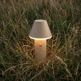 Trådløs beige Cone bordlampe fra sackit med varmt lys placeret i højt græs og skabt til hyggelige udendørs omgivelser det meste af året