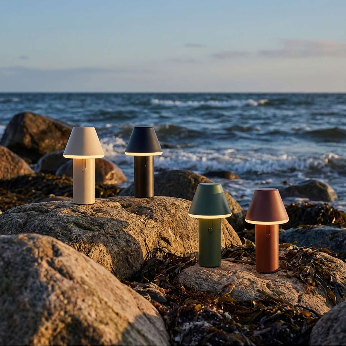 Fire trådløse Cone bordlamper fra sackit i forskellige farver står på klipper ved havet i nordisk aftenlys