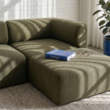 Olivegrøn Fjord sofa med matchende pouf i et lyst nordisk hjem med hvid murstensvæg naturligt lys bog og briller fra sackit
