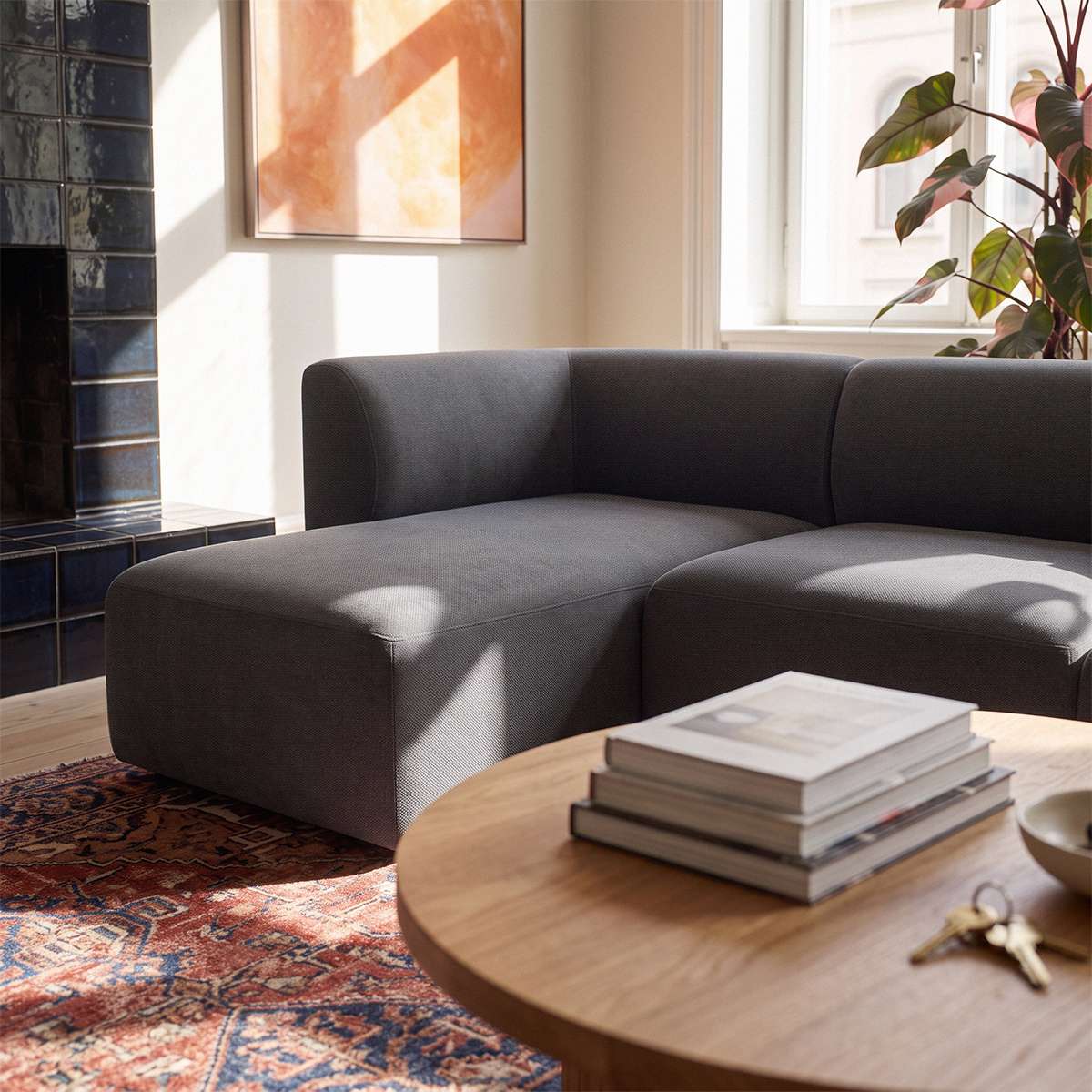 Mørkegrå Fjord sofa med venstrevendt chaiselong i lys nordisk stue med sofabord bøger plante kunst og farverigt vintage tæppe