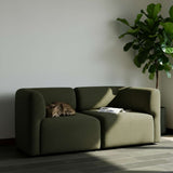 Grøn Fjord sofa til to personer i et lyst nordisk hjem med en kat på sædet og en stor grøn plante ved siden af
