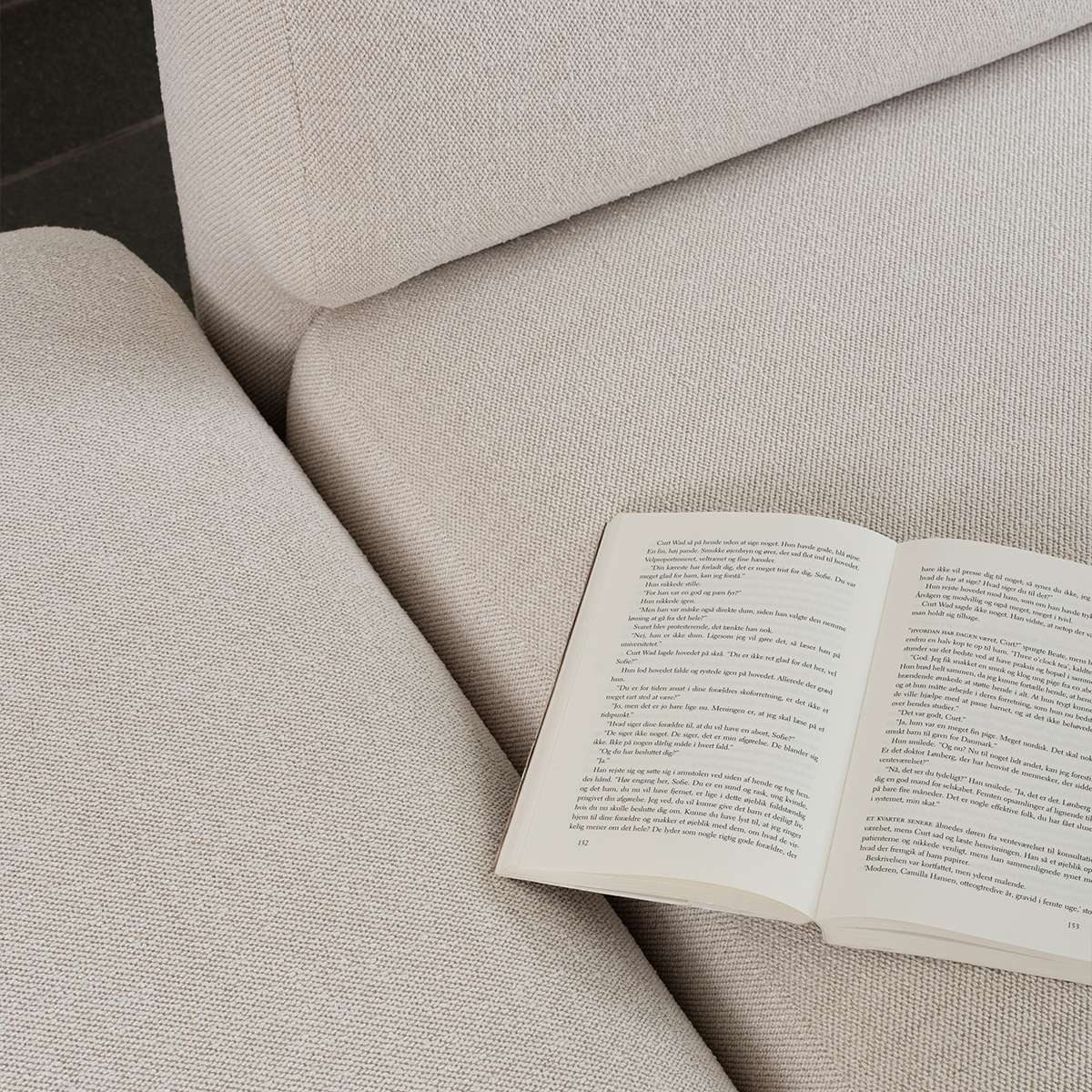 Fjord sofa i lyst tekstil med bløde polstrede former og en åben bog på sædet. Et roligt skandinavisk udtryk fra sackit