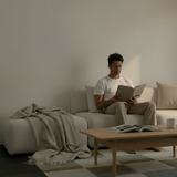 Skandinavisk hjørnesofa med åben ende i en rolig stue hvor en mand læser omgivet af bløde tekstiler træbord og naturlige nuancer