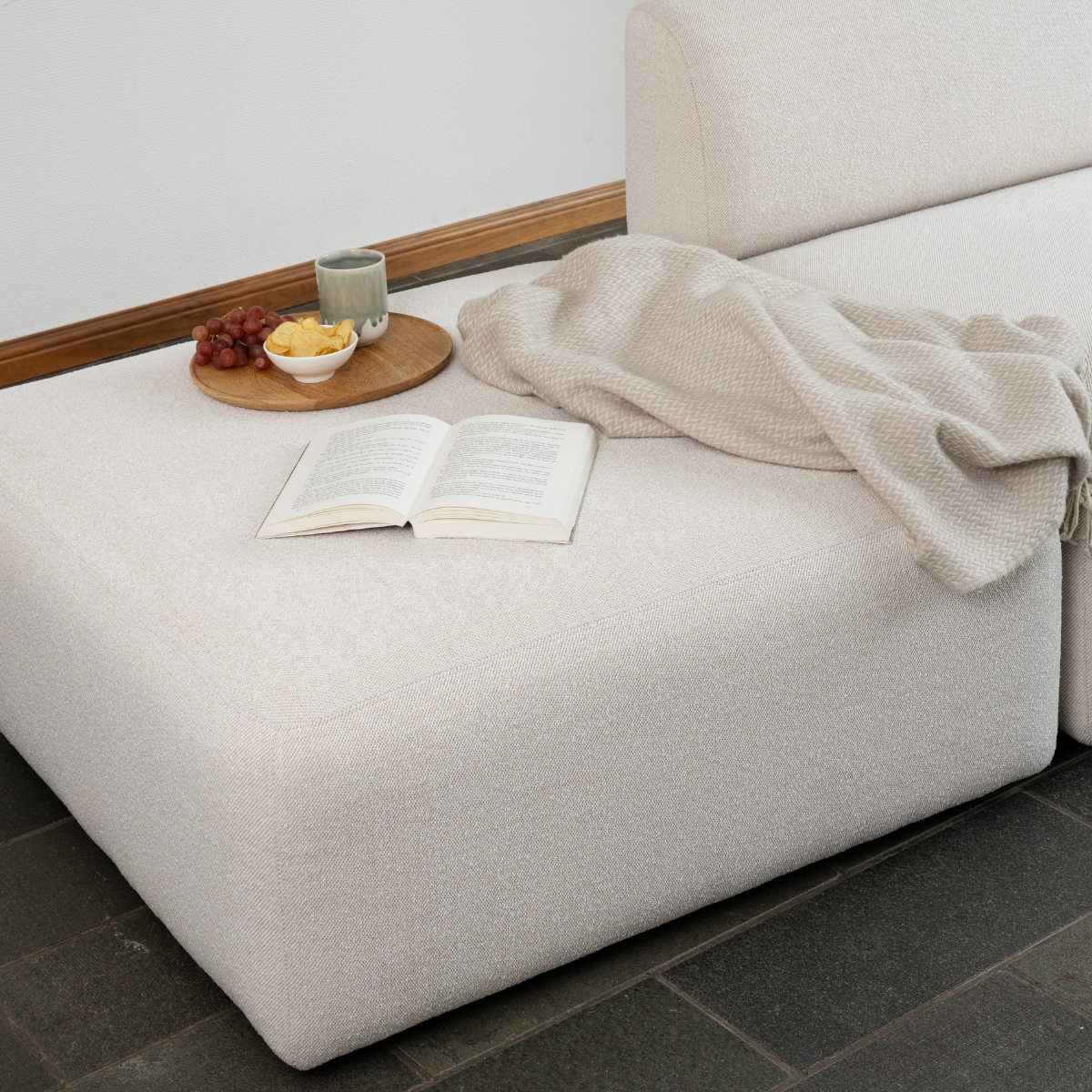 sackit Fjord sofa med åben ende i lyst tekstil med strikket tæppe åben bog og serveringsbakke med frugt i en rolig skandinavisk stue