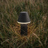 Sort trådløs udendørslampe fra sackit med varmt lys placeret blandt højt græs og vilde planter i den nordiske natur