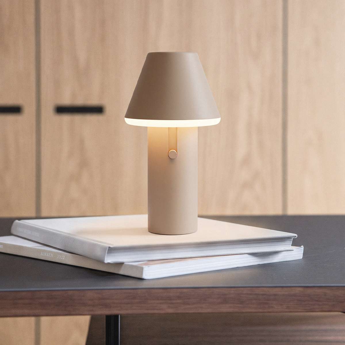 Beige trådløs Cone bordlampe fra sackit på en stak bøger på et mørkt træbord i et nordisk interiør