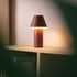 Brun trådløs bordlampe fra sackit med kegleformet skærm og varmt lys på en træhylde i et hyggeligt nordisk interiør