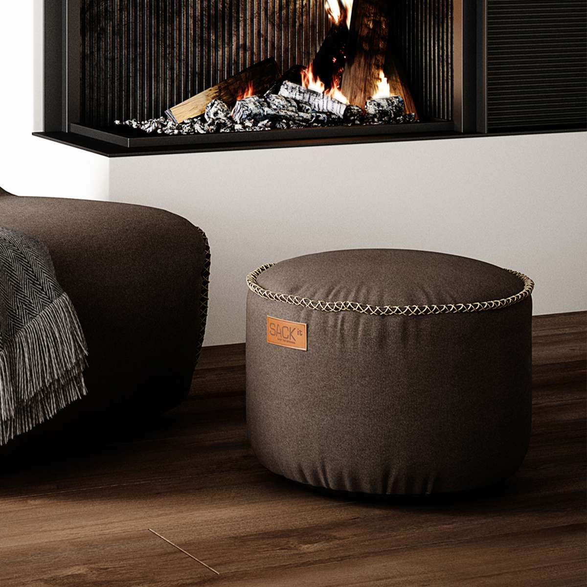 Brun rund Canvas Pouf fra sackit i tekstil placeret foran en pejs i en varm og stilfuld stue
