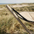 Detalje af beige Cobana hængekøje med stativ og sorte ophængsbånd i klitlandskab ved havet, med vanddråber på stoffet