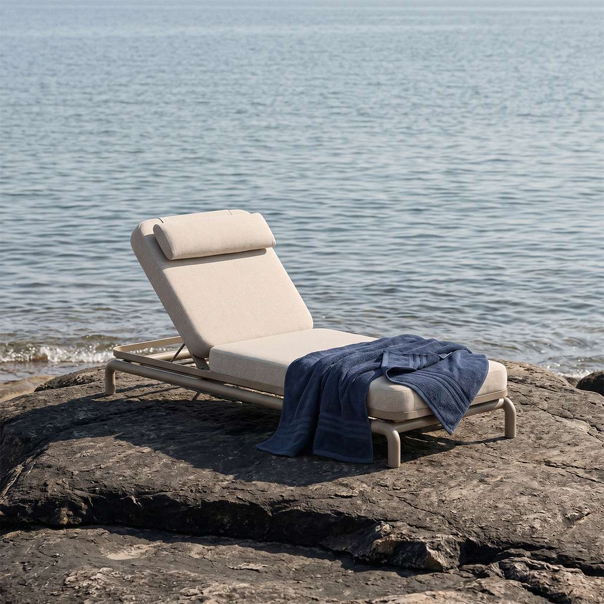 sackit Kirra solseng i lyst tekstil med justerbart ryglæn og mørk plaid på klipper ved havet omgivet af roligt nordisk kystlandskab