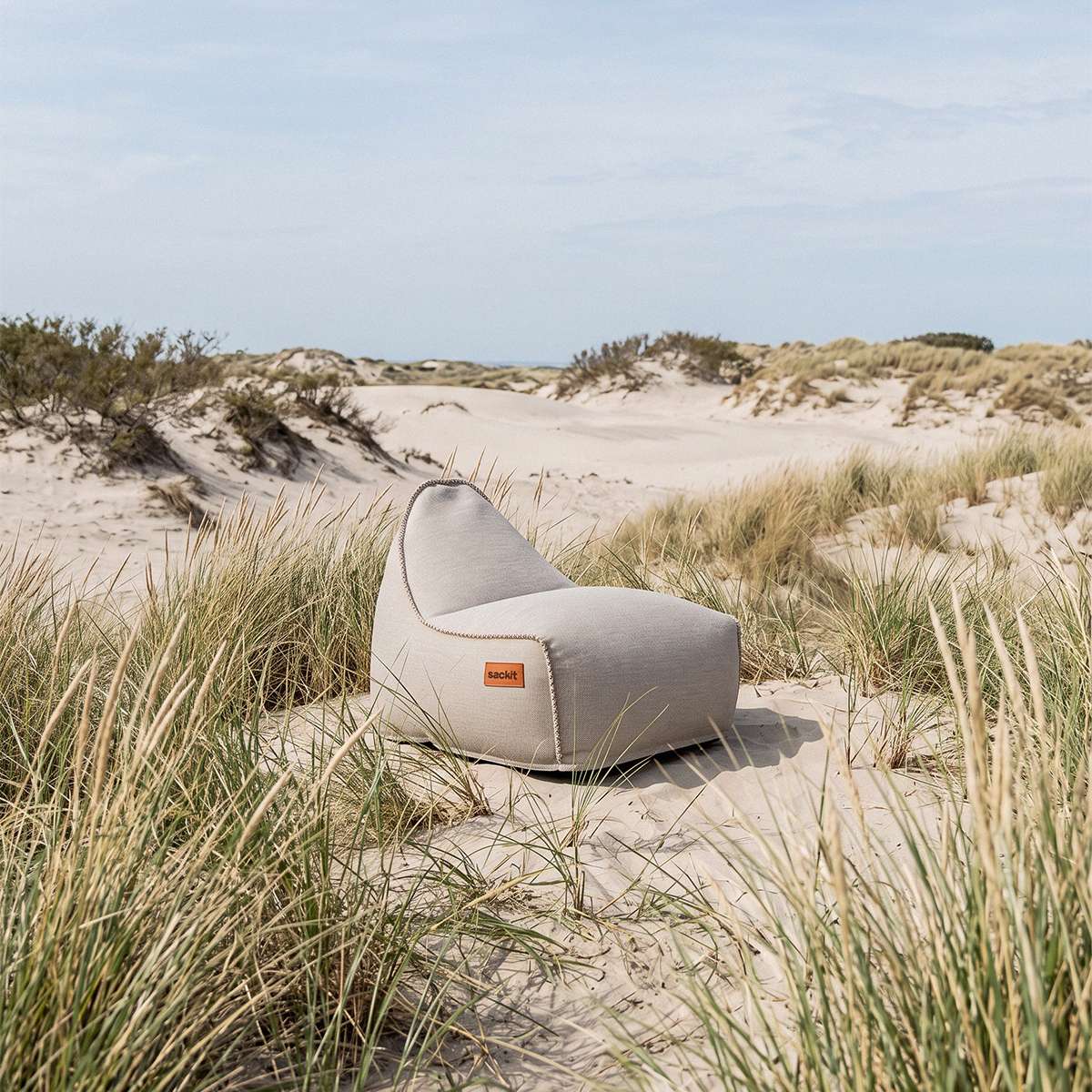 sackit Cobana loungestol i lysegråt stof placeret mellem marehalm og sandklitter ved kysten